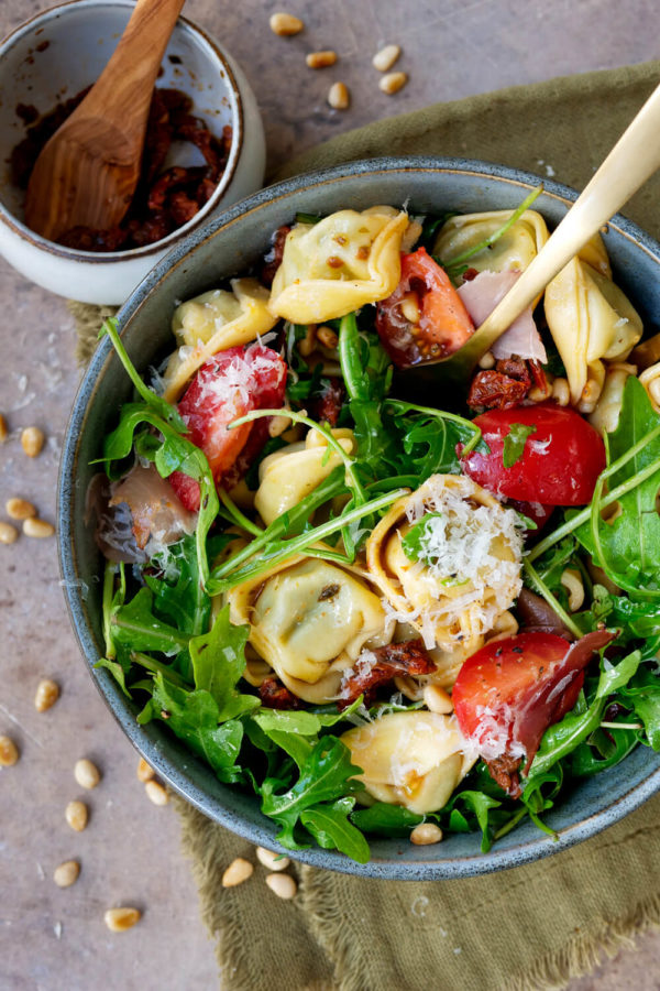 Tortellinisalat Rezept mit Parmesan, getrockneten Tomaten, Schinken, Rucola und Pinienkernen