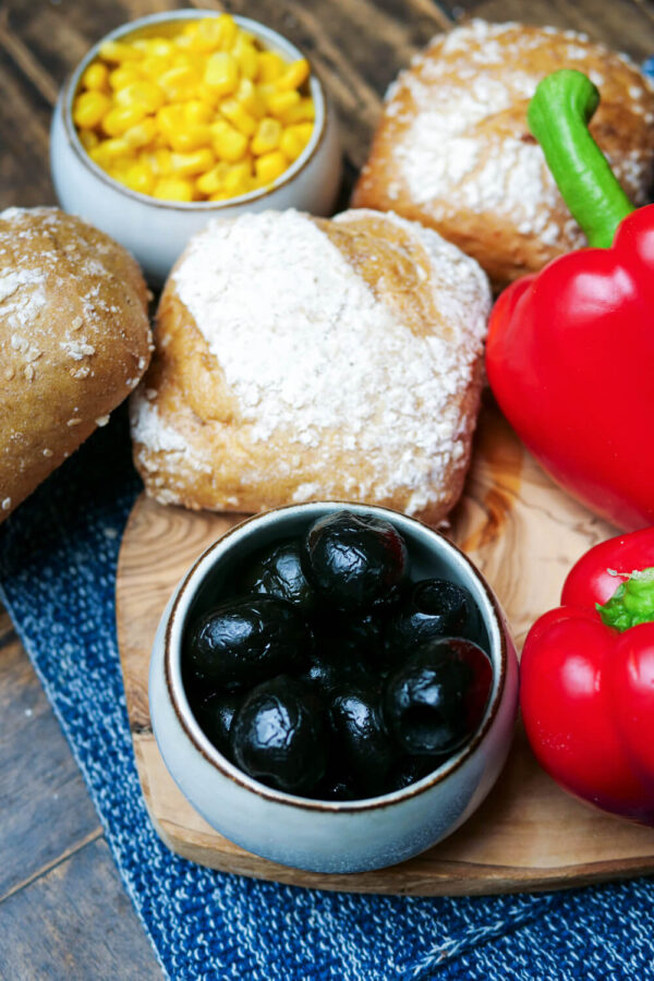 Oliven, Brötchen, Paprika und Mais auf einem Holzbrett.