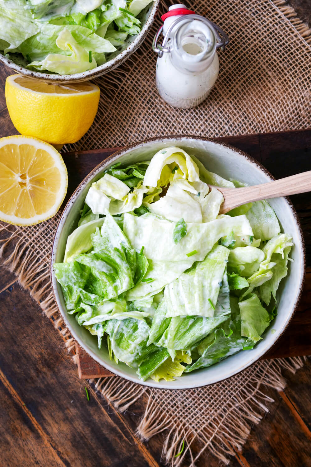 Eisbergsalat mit Dressing in einer Salatschüssel mit Holzlöffel.