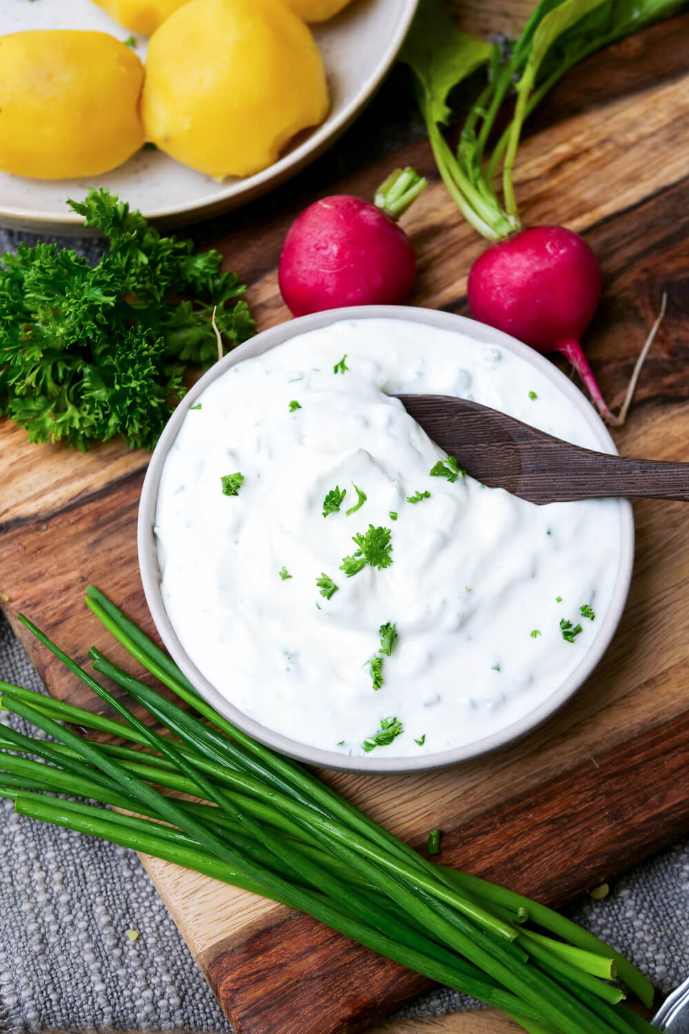 Quark-Dip in einem Schälchen mit Holzlöffel und Schnittlauch und Radieschen angelegt.