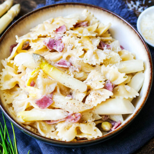 Pasta mit weißem Spargel und Schinken auf einem Teller angerichtet mit angelegter Gabel.