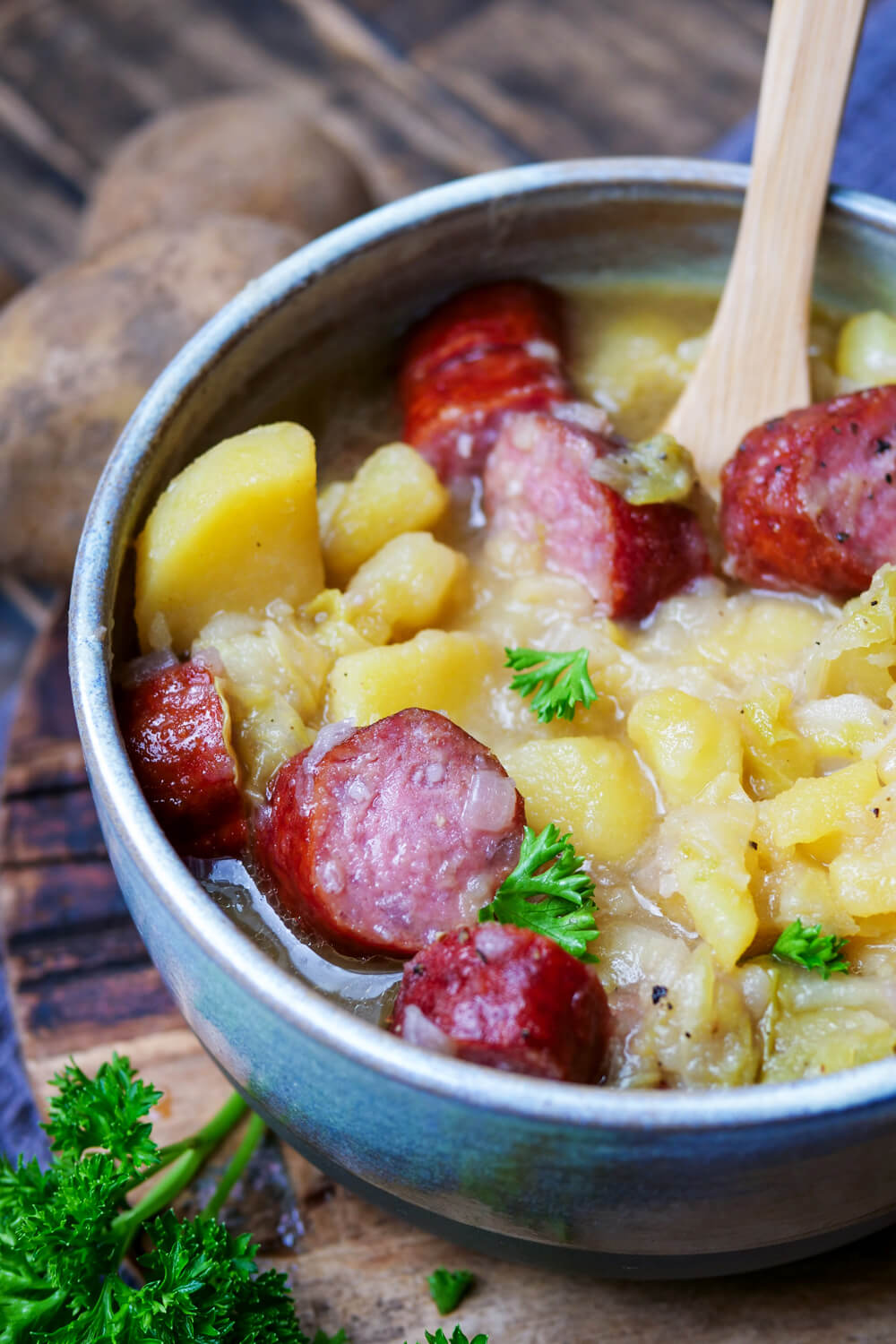 Spitzkohl-Kartoffel-Eintopf mit Mettenden in einer Schüssel mit Holzlöffel.