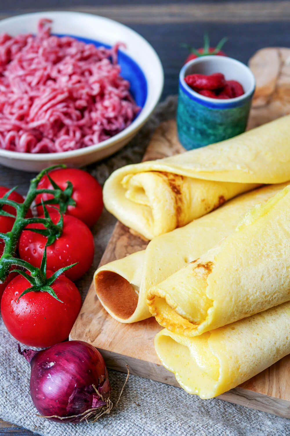 Pfannkuchen, Zwiebel, Tomaten, Hackfleisch und Tomatenmark auf einem Holzbrett.