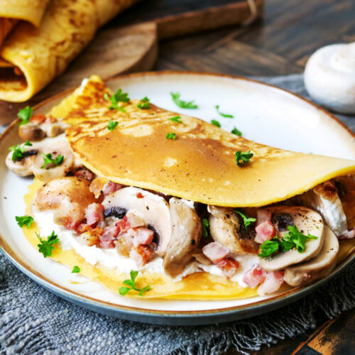 Gefüllter Pfannkuchen mit Champignons und Speck auf einem Teller.