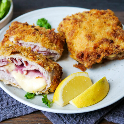 Cordon Bleu aus der Heißluftfritteuse angeschnitten und im Ganzen auf einem Teller mit Zitrone.