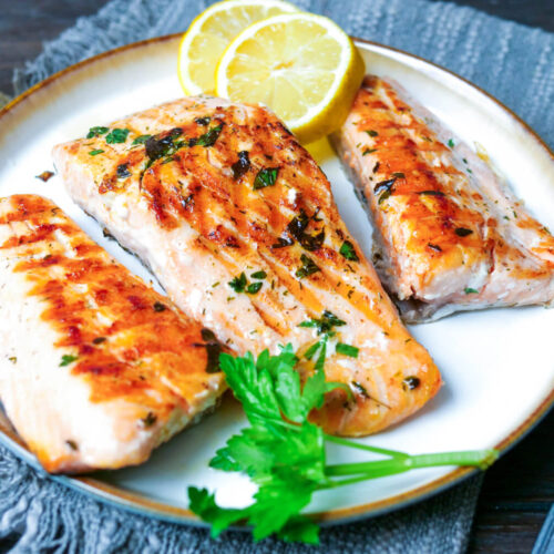 Gegrillte Lachsfilet auf einem Teller mit Petersilie und Zitrone.