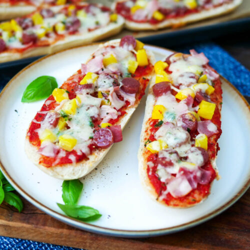 Zwei Pizza-Baguettes auf einem Teller mit Basilikumblättchen.