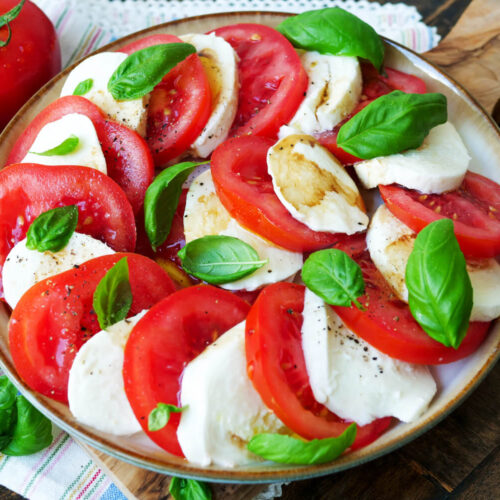 Tomate-Mozzarella mit Basilikum auf einem Teller.