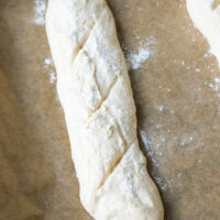 Rohes Baguette auf einem Backblech mit Backpapier.