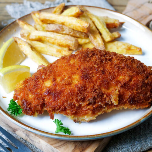 Hähnchen-Cordon-Bleu mit Pommes und Zitronenspalten auf einem Teller.