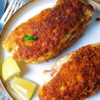 Zwei Hähnchen-Cordon-Bleu mit Zitronenspalten auf einem Teller.