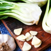 Halbierter Pak Choi und Knoblauchscheiben auf einem Holzbrett.