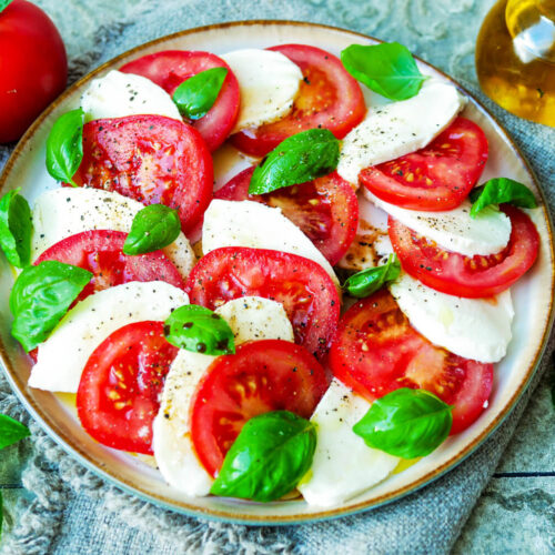 Tomate-Mozzarella mit Basilikum auf einem Teller.