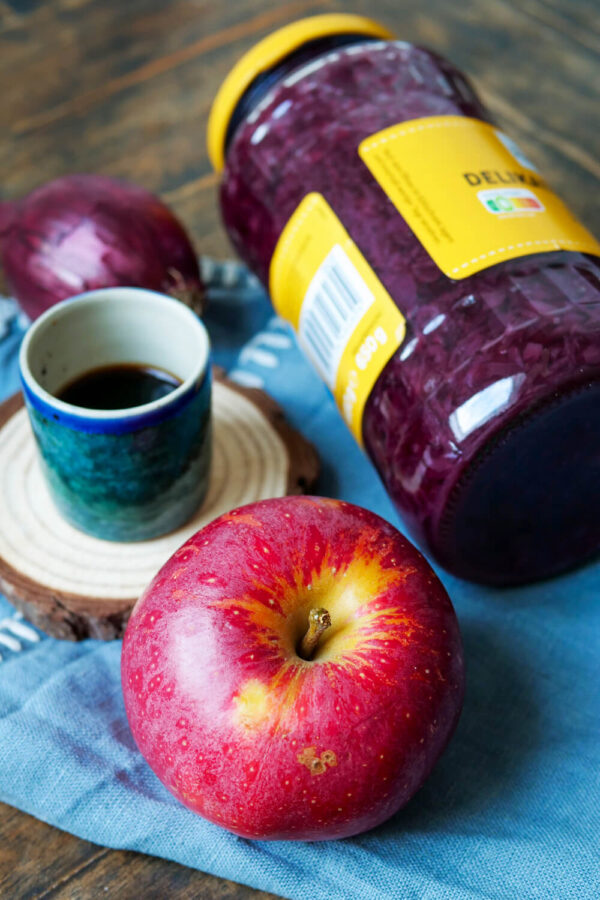 Apfel, Balsamico-Essig und Rotkohl im Glas auf einem blauen Tuch.