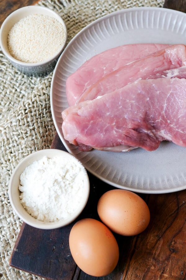 Die Zutaten für Schnitzel auf einem Holzbrett angerichtet.