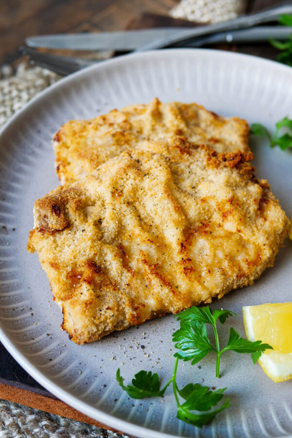 Schnitzel aus der Heißluftfritteuse auf einem Teller mit Petersilie und Zitronenstück.