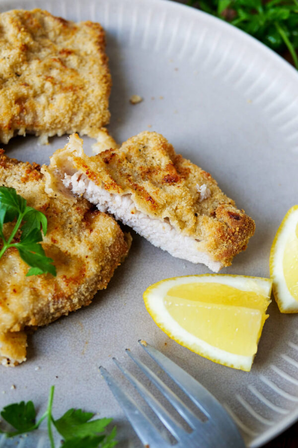 Panierte Schnitzel auf einem Teller mit Zitrone und Gabel.