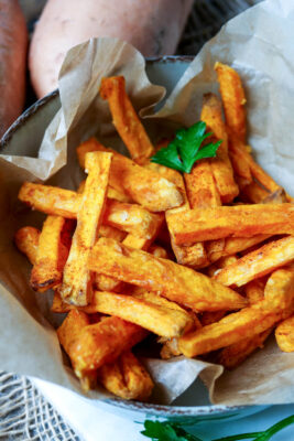 Süßkartoffel-Pommes aus der Heißluftfritteuse in einer Schale mit Backpapier.