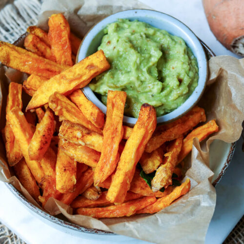 Süßkartoffel-Pommes aus der Heißluftfritteuse mit Avocadocreme in einer Schale.