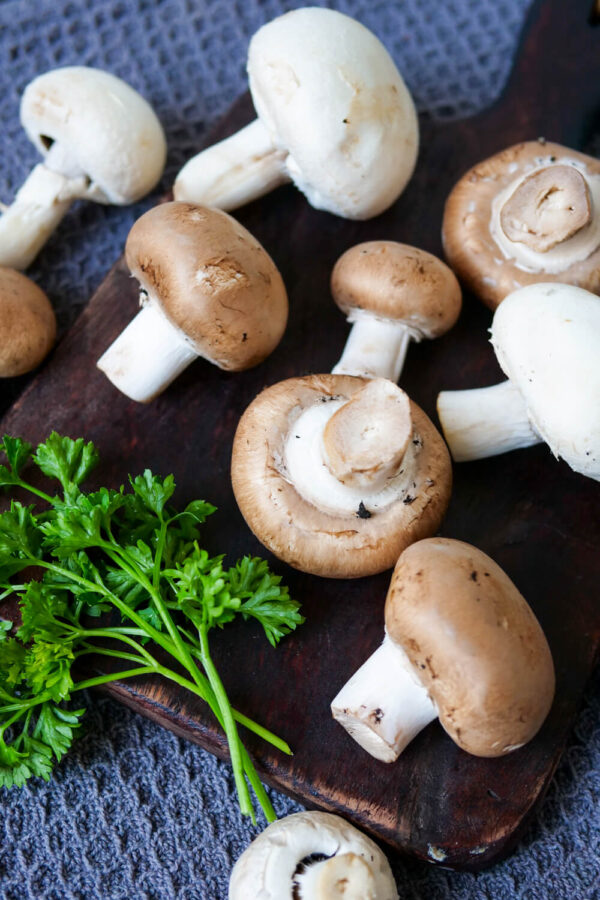 Frische Champignons auf einem dunklen Brettchen.