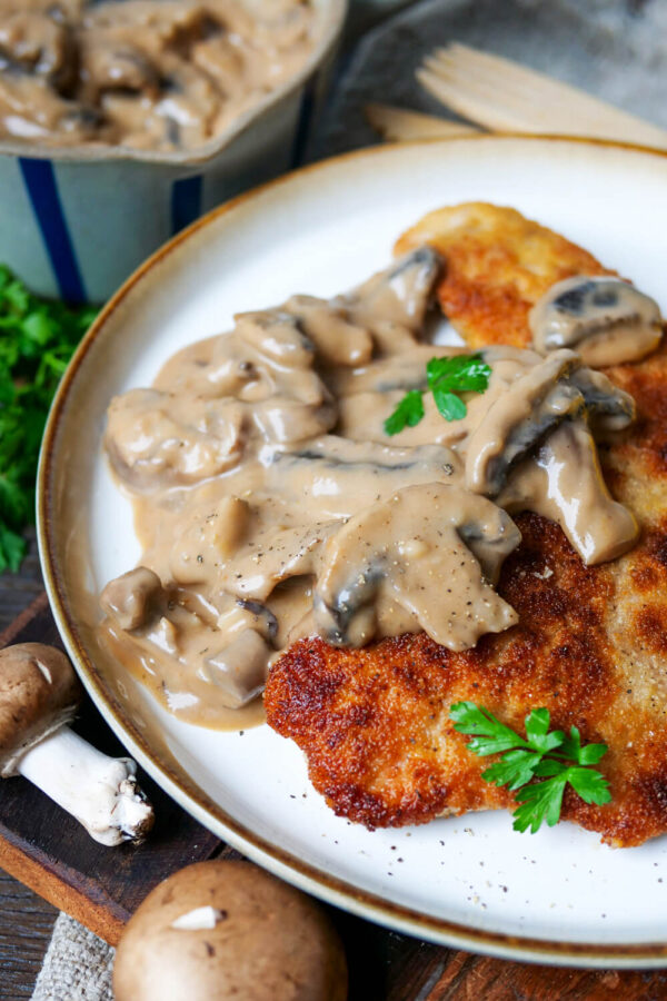 Jägerschnitzel paniert mit Soße auf einem weißen Teller.