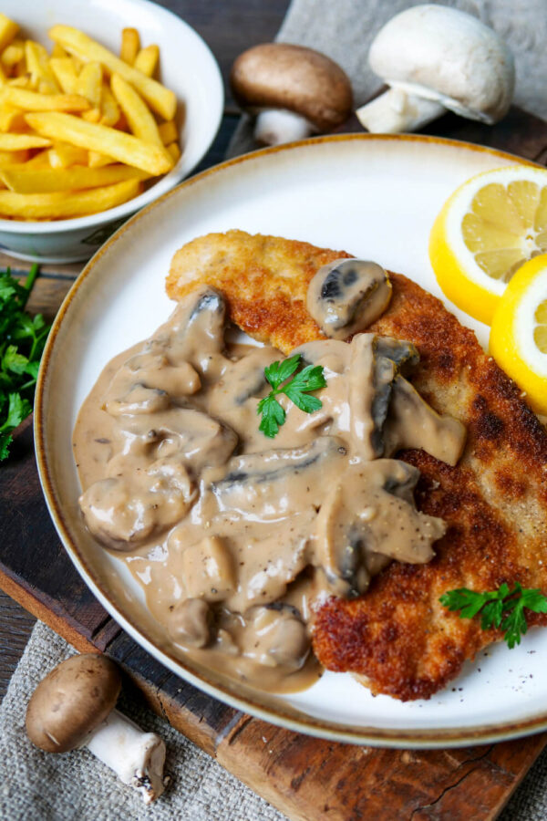 Jägerschnitzel mit Soße und Zitrone auf einem weißen Teller.