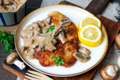 Jägerschnitzel mit Soße und Zitrone auf einem weißen Teller.