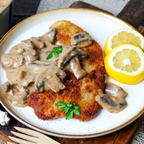 Jägerschnitzel mit Soße und Zitrone auf einem weißen Teller.