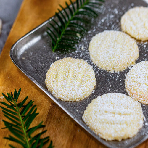 Schneeflocken-Plätzchen mit Tannenzweig auf einem silbernen Teller.