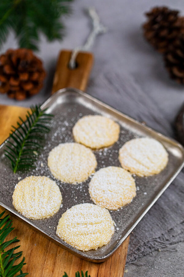 Schneeflocken-Plätzchen auf einem silbernen Teller mit Tannenzweig.